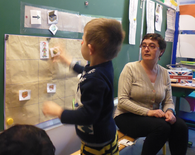 Kind mit Lehrerin und dem an der Tafel angebrachten Schatzsuche-Spiel