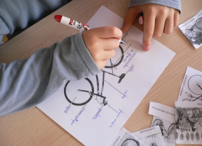 Foto: Ein Kind beschriftet eine Zeichnung (Bauteile eines Fahrrads)